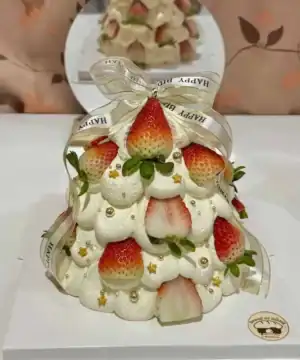 เค้กต้นคริสต์มาสหวานอร่อย ตกแต่งด้วยสตรอว์เบอร์รีและครีมสด พร้อมริบบิ้นทองคำ.