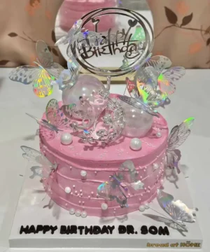 เค้กวันเกิดสีชมพูหวาน พร้อมตกแต่งด้วยผีเสื้อเรืองแสงและลูกปัด สื่อความสุขและความสนุกในโอกาสพิเศษ.