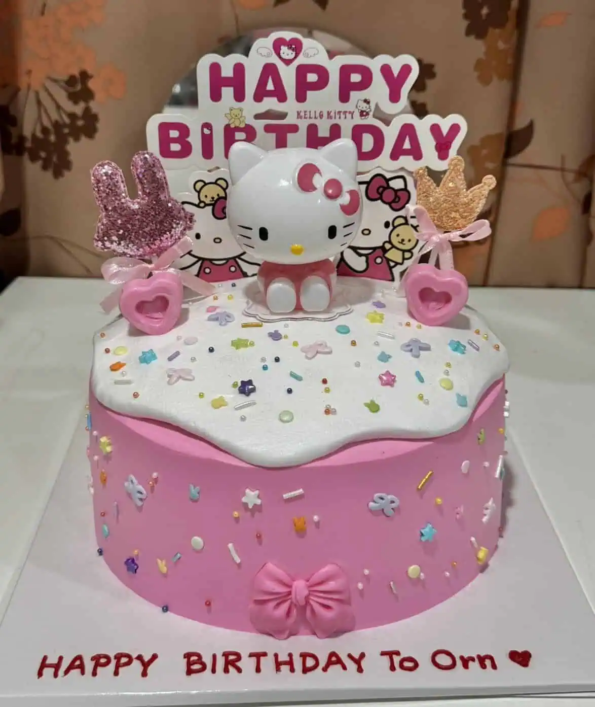 เค้กวันเกิดคิตตี้สีชมพูพร้อมตกแต่งด้วยตัวการ์ตูน Hello Kitty และของตกแต่งน่ารัก เช่น ร็อคกี้และหัวใจ.