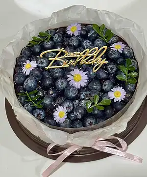 เค้กบลูเบอร์รี่ชีสพายตกแต่งด้วยบลูเบอร์รี่สด ดอกไม้และคำว่า Happy Birthday บนห.
