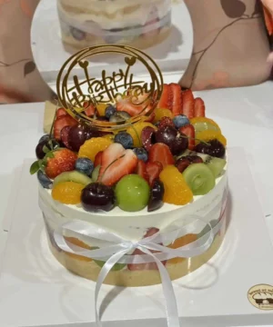 เค้กผลไม้สดรวมหน้าตาน่ารับประทาน ประดับด้วยผลไม้สดหลากหลายชนิด เช่น สตรอเบอร์รี่ บลูเบอร์รี่ องุ่น และส้ม พร้อมคำอวยพรวันเกิด.