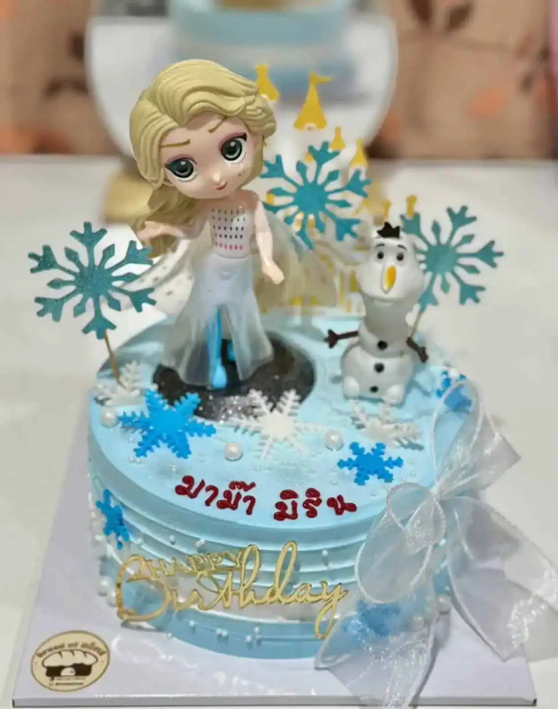 เค้กวันเกิดเจ้าหญิงน้ำแข็ง Elsa พร้อมตัวการ์ตูน Olaf และหิมะน้ำแข็งตกแต่งบนเค้กสีฟ้า.