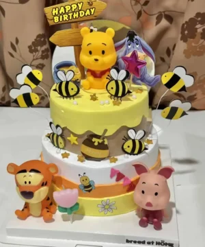 นกผึ้งและตัวการ์ตูน Winnie the Pooh กับอาหารเค้กวันเกิดสำหรับเด็ก, เค้กน่ารักตกแต่งด้วยตัวการ์ตูนและลูกโป่ง, เหมาะสำหรับปาร์ตี้วันเกิดเด็ก, ข้อเสนอการออกแบบเค้กสนุกสนานและน่ารัก, โฟกัสคำค้นหาเค้กวันเกิดและการตกแต่งสำหรับงานเลี้ยงเด็ก.