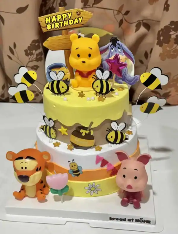 นกผึ้งและตัวการ์ตูน Winnie the Pooh กับอาหารเค้กวันเกิดสำหรับเด็ก, เค้กน่ารักตกแต่งด้วยตัวการ์ตูนและลูกโป่ง, เหมาะสำหรับปาร์ตี้วันเกิดเด็ก, ข้อเสนอการออกแบบเค้กสนุกสนานและน่ารัก, โฟกัสคำค้นหาเค้กวันเกิดและการตกแต่งสำหรับงานเลี้ยงเด็ก.