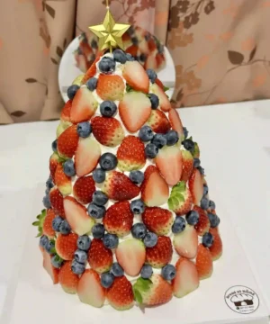 กล่องผลไม้และเค้กผลไม้ตกแต่งสำหรับงานปาร์ตี้คริสต์มาส, เค้กผลไม้สดบนโทนสีแดงและน้ำเงิน, สร้างสรรค์ด้วยผลไม้สดและตกแต่งด้วยดาวทอง, เค้กผลไม้สดสำหรับโอกาสพิเศษ, การตกแต่งเค้กผลไม้สดด้วยสตรอเบอร์รี่, บลูเบอร์รี่และผลไม้อื่น ๆ เพื่อความสวยงามและรสชาติอร่อย.