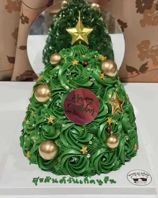 เค้กต้นคริสต์มาสสีเขียวประดับด้วยลูกบอลทองและดาวทอง พร้อมข้อความสุขสันต์วันคริสต์มาส.