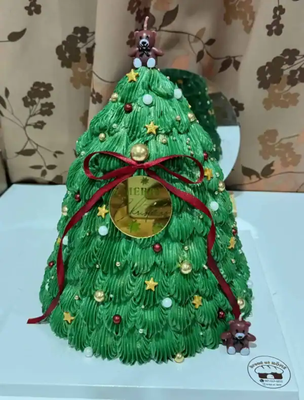 เค้กต้นคริสต์มาสตกแต่งด้วยไอเท็มคริสต์มาสสีเขียวสดใส พร้อมลูกบอลและริบบิ้นแดง เหมาะสำหรับงานเฉลิมฉลองในช่วงเทศกาลคริสต์มาส.