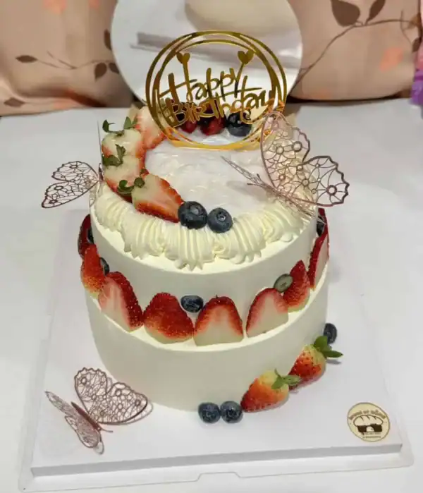 เค้กผลไม้สดวันเกิดตกแต่งด้วยสตรอเบอร์รี่ บลูเบอร์รี่ และครีมสด พร้อมป้าย Happy Birthday บนยอดเค้ก.