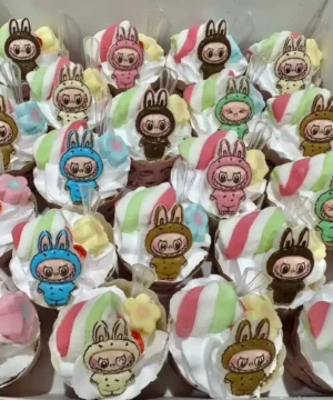 คัพเค้กลายการ์ตูนสุดน่ารักตกแต่งด้วยวิปครีมและช็อกโกแลต พร้อมตัวการ์ตูนลายคัพเค้กน่ารักในธีมสุดฮิต เหมาะสำหรับงานปาร์ตี้และของขวัญพิเศษ.