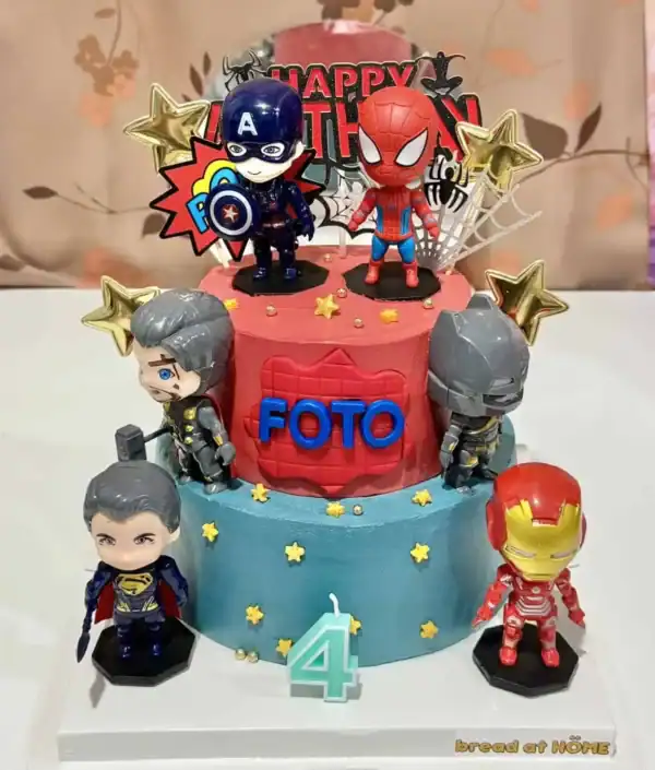 เค้กวันเกิดสองชั้นตกแต่งด้วยตัวการ์ตูนซุปเปอร์ฮีโร่จาก Marvel และ DC พร้อมของตกแต่งทองคำและดาวสีทอง.