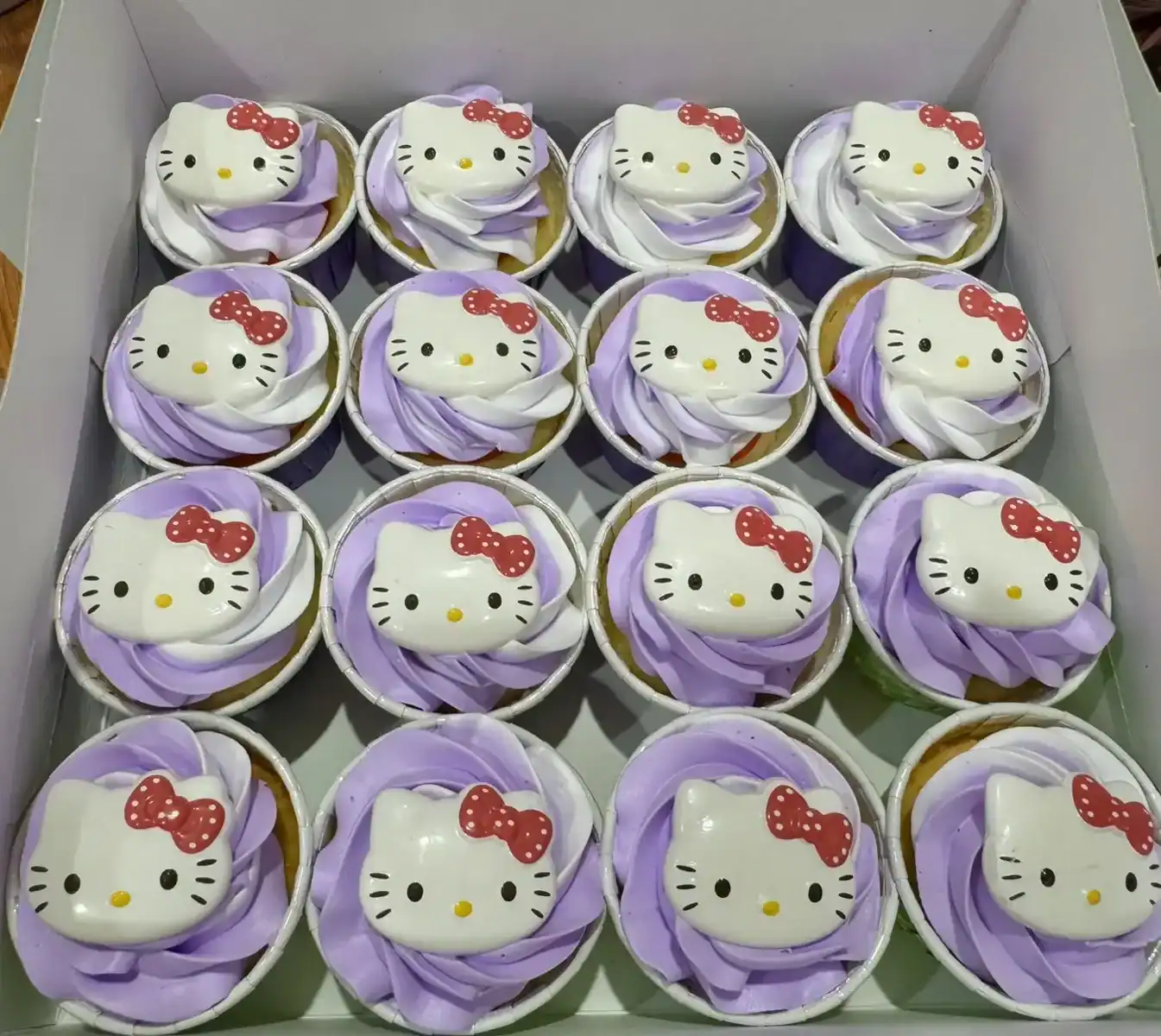 คัพเค้กคิตตี้ Hello Kitty สีขาวและม่วง พร้อมตกแต่งด้วยหน้าคิตตี้และโบว์แดง.