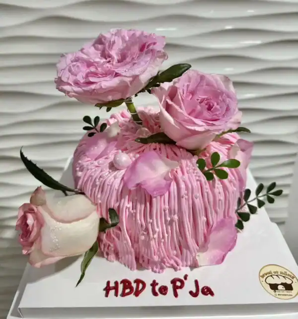 เค้กดอกไม้สีชมพูหวาน พร้อมตกแต่งด้วยดอกไม้และใบเขียว สวยงาม เหมาะสำหรับงานฉลองและโอกาสพิเศษ.