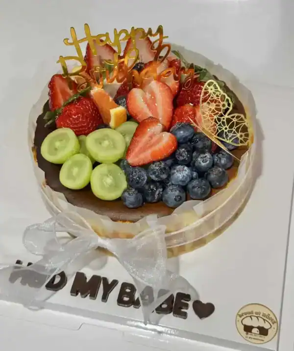 เค้กผลไม้สดตกแต่งด้วยสตรอเบอร์รี่ กล้วย บลูเบอร์รี่ และแตงโม พร้อมคำว่า Happy Birthday บนยอดเค้ก.