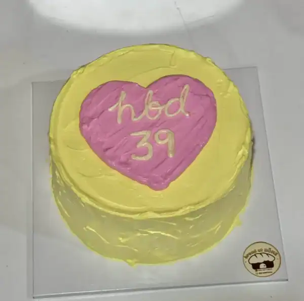 เค้กวันเกิดสีเหลืองสดใสพร้อมหัวใจสีชมพูเขียนคำว่า 'hbd 39' สำหรับโอกาสพิเศษ.