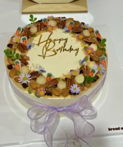 เค้กแครอทเนื้อเนียนนุ่ม พร้อมครีมชีสหวานมัน ตกแต่งด้วยดอกไม้และถั่วหลากสี สวยงามเหมาะสำหรับฉลองวันเกิดหรือโอกาสพิเศษ.