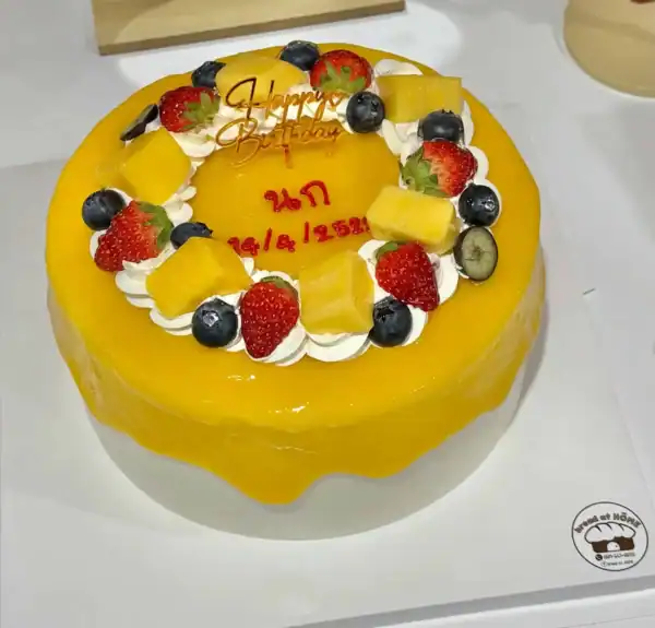 เค้กมะม่วงสดหวานหอม topped ด้วยผลไม้สด เช่น สตรอว์เบอร์รี บลูเบอร์รี กีวี และสับปะรด พร้อมครีมสดเนียนนุ่มสำหรับงานฉลองพิเศษ.