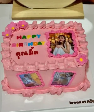 เค้กวันเกิดสีชมพูตกแต่งด้วยดอกไม้และภาพถ่ายของเด็กหญิงในโอกาสพิเศษ พร้อมข้อความสุขสันต์วันเกิดและชื่อ.