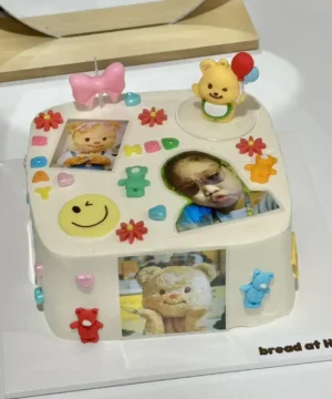 ภาพเค้กวันเกิดตกแต่งด้วยภาพถ่ายและของตกแต่งน่ารัก ตกแต่งด้วยลูกอม ดอกไม้ และตัวการ์ตูนสีสันสดใส สื่อถึงความสุขและความสนุกในโอกาสพิเศษสำหรับเด็ก ๆ.