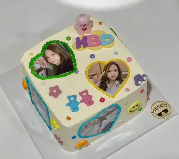 เค้กวันเกิดรูปหัวใจตกแต่งด้วยภาพถ่ายและตัวอักษร HBD พร้อมของตกแต่งน่ารัก เช่น ตุ๊กตาและดอกไม้.