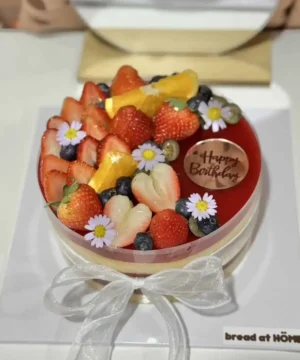 กล่องเค้กผลไม้สด สักเป็นเค้กวันเกิด พร้อมดอกไม้และแผ่นตัดข้อความสุขสันต์วันเกิดสำหรับโอกาสพิเศษในครอบครัวหรือโอกาสสำคัญ.