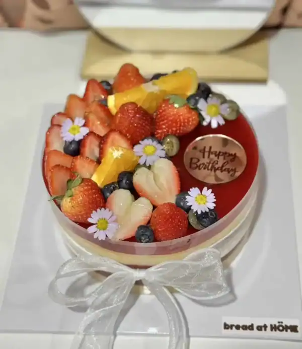 กล่องเค้กผลไม้สด สักเป็นเค้กวันเกิด พร้อมดอกไม้และแผ่นตัดข้อความสุขสันต์วันเกิดสำหรับโอกาสพิเศษในครอบครัวหรือโอกาสสำคัญ.