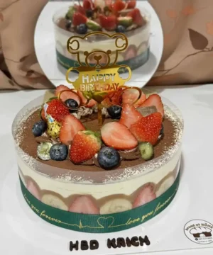 เค้กผลไม้สดหวานฉ่ำตกแต่งด้วยสตรอเบอร์รี่ บลูเบอร์รี่ และผลไม้สดอื่น ๆ บนเค้กช็อกโกแลตเนียนนุ่ม พร้อมคำอวยพรวันเกิดและการตกแต่งน่ารัก.