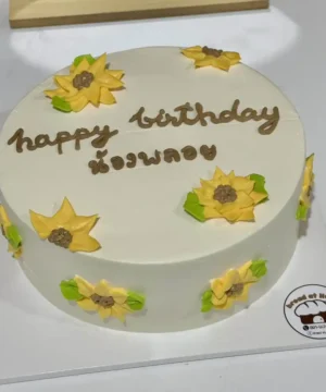 ชุดเค้กวันเกิดทำเองในบ้าน ทรงกลมสีขาวพร้อมดอกไม้ตกแต่งสีเหลืองและเขียว ในโอกาสฉลองวันเกิดที่บ้านเพื่อสร้างความทรงจำดีๆ.