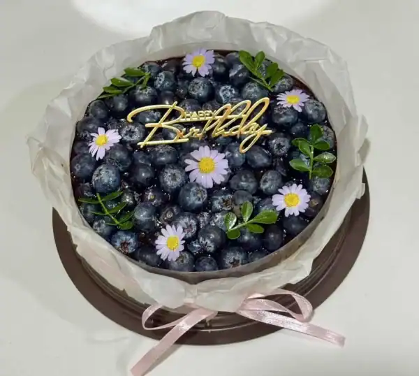เค้กบลูเบอร์รี่ชีสพายตกแต่งด้วยบลูเบอร์รี่สด ดอกไม้และคำว่า Happy Birthday บนห.