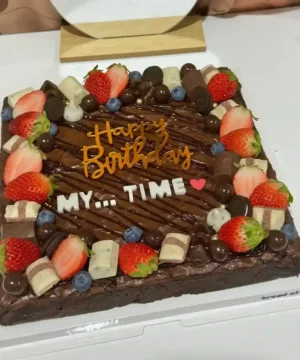 เค้กบราวนี่เนื้อแน่นหนึบ พร้อมตกแต่งด้วยผลไม้สด ช็อกโกแลต และคำอวยพรวันเกิด สร้างบรรยากาศพิเศษสำหรับโอกาสสำคัญ.