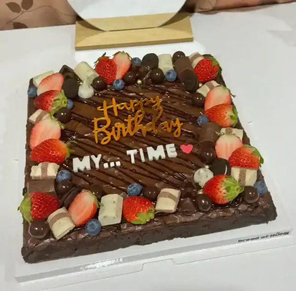 เค้กบราวนี่เนื้อแน่นหนึบ พร้อมตกแต่งด้วยผลไม้สด ช็อกโกแลต และคำอวยพรวันเกิด สร้างบรรยากาศพิเศษสำหรับโอกาสสำคัญ.