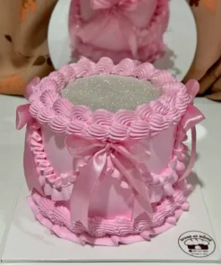 เค้กกลิตเตอร์สีชมพูหวาน พร้อมตกแต่งด้วยริบบิ้นและลายลูกไม้ สร้างความโดดเด่นและเปล่งประกายในทุกงานฉลองด้วยความสวยงามและความหรูหรา.