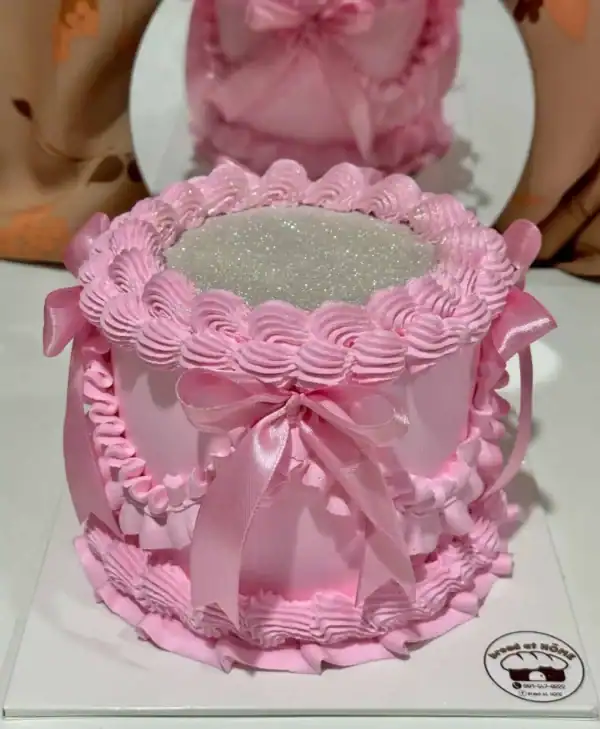 เค้กกลิตเตอร์สีชมพูหวาน พร้อมตกแต่งด้วยริบบิ้นและลายลูกไม้ สร้างความโดดเด่นและเปล่งประกายในทุกงานฉลองด้วยความสวยงามและความหรูหรา.
