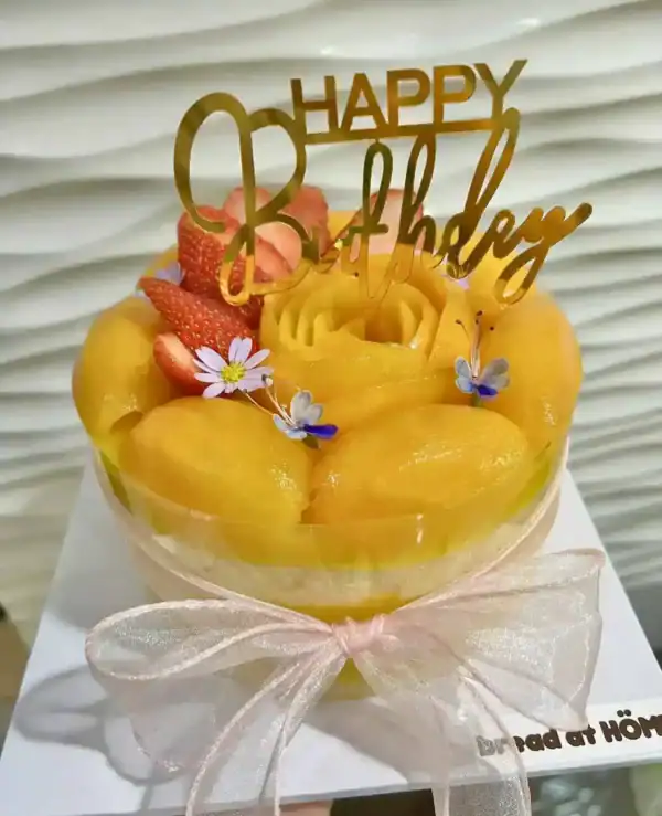 เค้กมะยงชิดสดหวานฉ่ำ เนื้อแน่น รสชาติเป็นเอกลักษณ์ พร้อมตกแต่งด้วยดอกไม้และคำอวยพรวันเกิด.