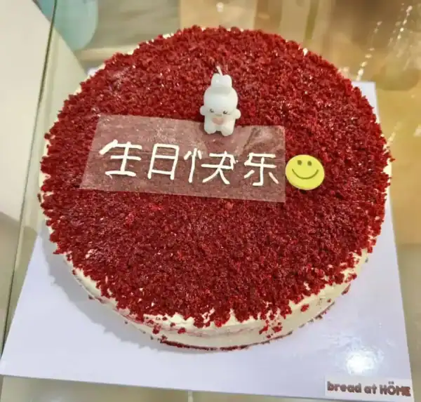 เค้กเรดเวลเวทเนื้อเนียนนุ่ม เคลือบด้วยผงโกโก้แดงสด พร้อมตกแต่งด้วยของตกแต่งน่ารักและข้อความในภาษาจีนบนหน้าเค้ก.
