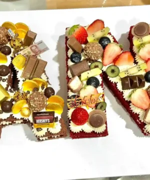 เค้กตัวอักษรทำเป็นชื่อเจ้าของวันเกิด ตกแต่งด้วยผลไม้สด ช็อกโกแลต และขนมหวานหลากหลายรสชาติ เหมาะสำหรับงานฉลองและสร้างความประทับใจให้กับผู้รับ.