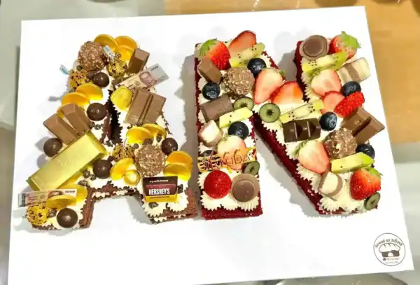 เค้กตัวอักษรทำเป็นชื่อเจ้าของวันเกิด ตกแต่งด้วยผลไม้สด ช็อกโกแลต และขนมหวานหลากหลายรสชาติ เหมาะสำหรับงานฉลองและสร้างความประทับใจให้กับผู้รับ.