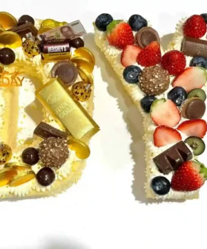 เค้กตัวอักษรวันเกิดทำจากครีมและผลไม้สด พร้อมตกแต่งด้วยช็อกโกแลตและขนมหวานหลากสี เหมาะสำหรับงานฉลองวันเกิดที่มีความหมายดีและดีไซน์เก๋ไก๋.