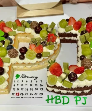 เค้กตัวอักษรวันเกิดดีไซน์เก๋ ตกแต่งด้วยผลไม้สดและช็อกโกแลต สร้างสรรค์เป็นชื่อเจ้าของวันเกิด พร้อมข้อความ HBD PJ สำหรับโอกาสพิเศษ.