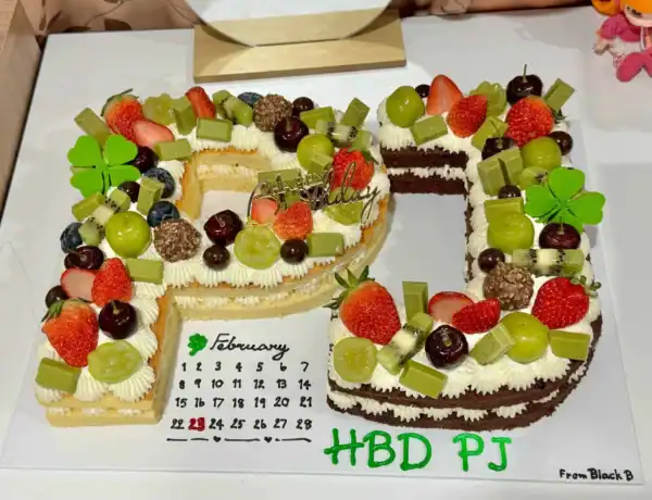 เค้กตัวอักษรวันเกิดดีไซน์เก๋ ตกแต่งด้วยผลไม้สดและช็อกโกแลต สร้างสรรค์เป็นชื่อเจ้าของวันเกิด พร้อมข้อความ HBD PJ สำหรับโอกาสพิเศษ.