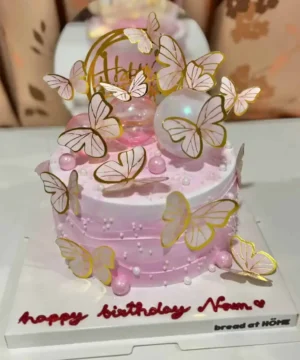 นกหวีดนางฟ้า เค้กวันเกิดสีชมพู บนตกแต่งด้วยผีเสื้อทองคำและลูกบอลใสมงคล สำหรับโอกาสพิเศษในบ้าน Bread at HÖME.