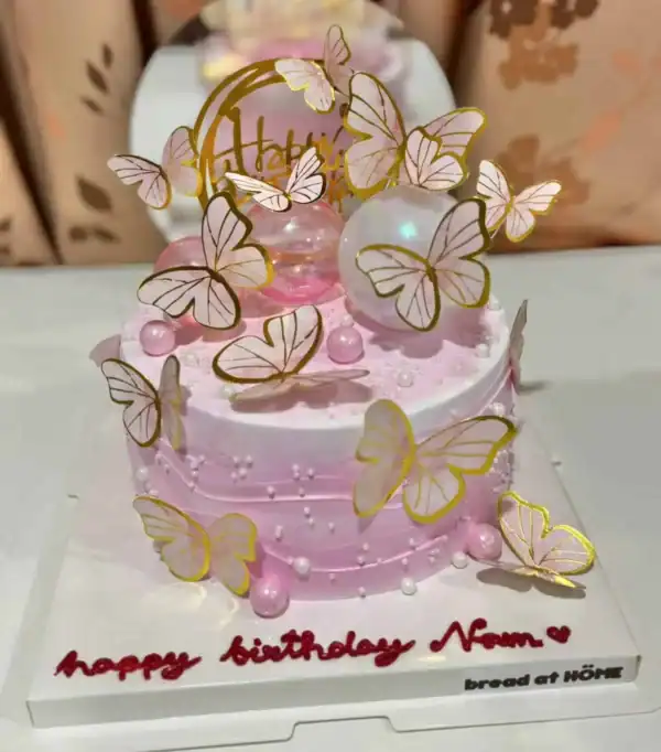 นกหวีดนางฟ้า เค้กวันเกิดสีชมพู บนตกแต่งด้วยผีเสื้อทองคำและลูกบอลใสมงคล สำหรับโอกาสพิเศษในบ้าน Bread at HÖME.