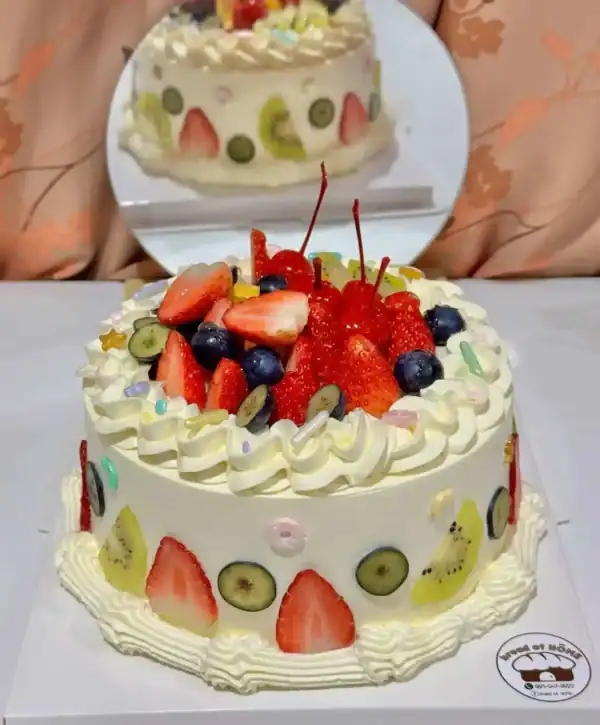 เค้กผลไม้สดรวมที่เต็มไปด้วยผลไม้หลากหลาย เช่น สตรอเบอร์รี่ กีวี บลูเบอร์รี่ และเชอร์รี่ บนเค้กเนื้อเนียนนุ่มตกแต่งด้วยครีมและลูกกวาดสีสันสดใส.
