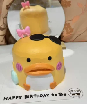 เค้กเป็ดน้อย 3 มิติสุดน่ารัก พร้อมแต่งด้วยแว่นตาและโบว์สีชมพู เหมาะสำหรับฉลองวันเกิดและโมเมนต์พิเศษต่าง ๆ.