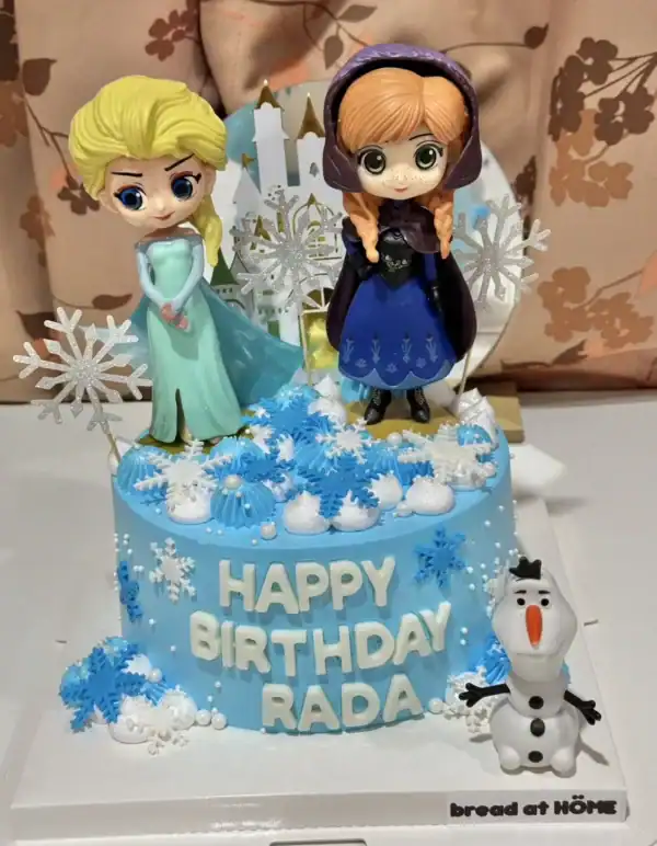 เค้กน้ำแข็งเจ้าหญิงเอลซ่าและอันนาสีฟ้าสดใส พร้อมตกแต่งด้วยหิมะเทียมและตัวการ์ตูนจากภาพยนตร์ดัง.