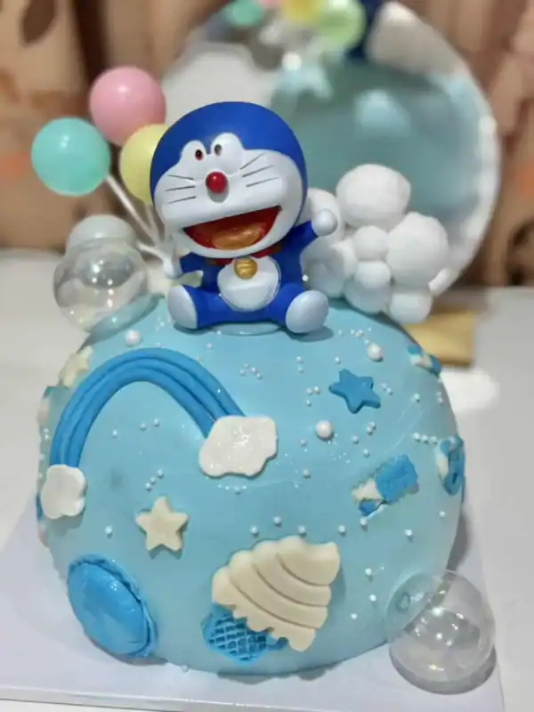 เทียนเค้กวันเกิดสีฟ้าพร้อมของตกแต่งรูปการ์ตูนโดราเอม่อนและท้องฟ้าในธีมสายรุ้งและก้อนเมฆ สร้างบรรยากาศสนุกสนานในงานปาร์ตี้วันเกิดของเด็กๆ.