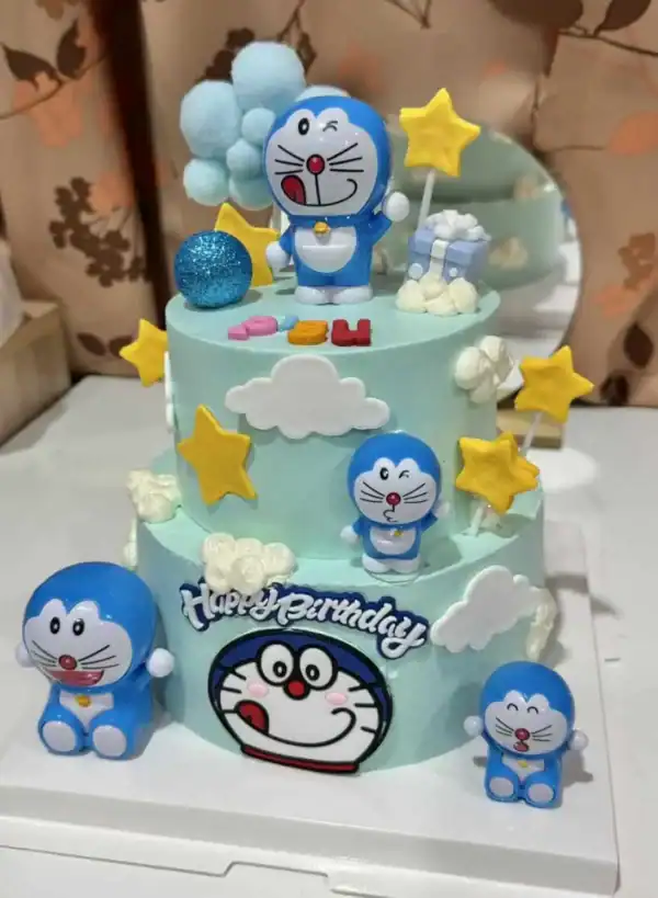 เค้กโดเรมอนสีฟ้าสดใสพร้อมตกแต่งด้วยดาวและเมฆน่ารัก เหมาะสำหรับฉลองวันเกิดหรือโอกาสพิเศษของแฟนคลับโดเรมอนทุกวัย.