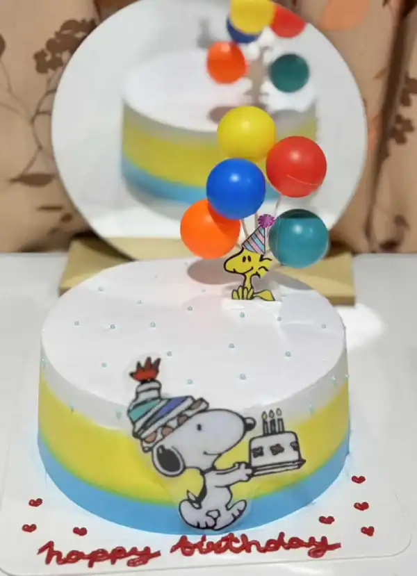 ขนมเค้กวันเกิด Snoopy กับลูกโป่งสีสันสดใสสำหรับงานเลี้ยงวันเกิด, สร้างบรรยากาศสนุกสนานและเปลี่ยนแปลงในงานฉลองที่บ้าน, สัญลักษณ์แห่งความสุขและความสนุกในโอกาสพิเศษ.