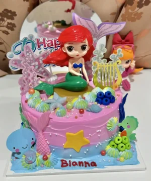 เค้กนางเงือกแอเรียลสีชมพูสดใส พร้อมตัวการ์ตูนแอเรียลและของตกแต่งทะเลน่ารัก เหมาะสำหรับงานวันเกิดเด็กผู้หญิงที่ชื่นชอบเทพนิยายและโลกใต้ทะเล.