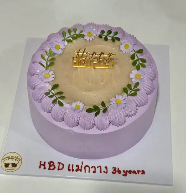 เค้กเผือกมะพร้าวอ่อนตกแต่งด้วยดอกไม้และใบไม้สีเขียวบนพื้นขาว พร้อมคำว่า Happy Birthday.
