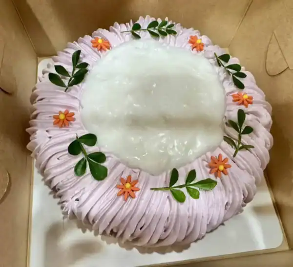เค้กเผือกมะพร้าวอ่อนเนื้อเนียนนุ่ม ตกแต่งด้วยดอกไม้และใบไม้สีเขียว สวยงาม เหมาะสำหรับของขวัญวันเกิดและโอกาสพิเศษ.